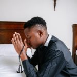 man in black dress shirt kneeling on bed